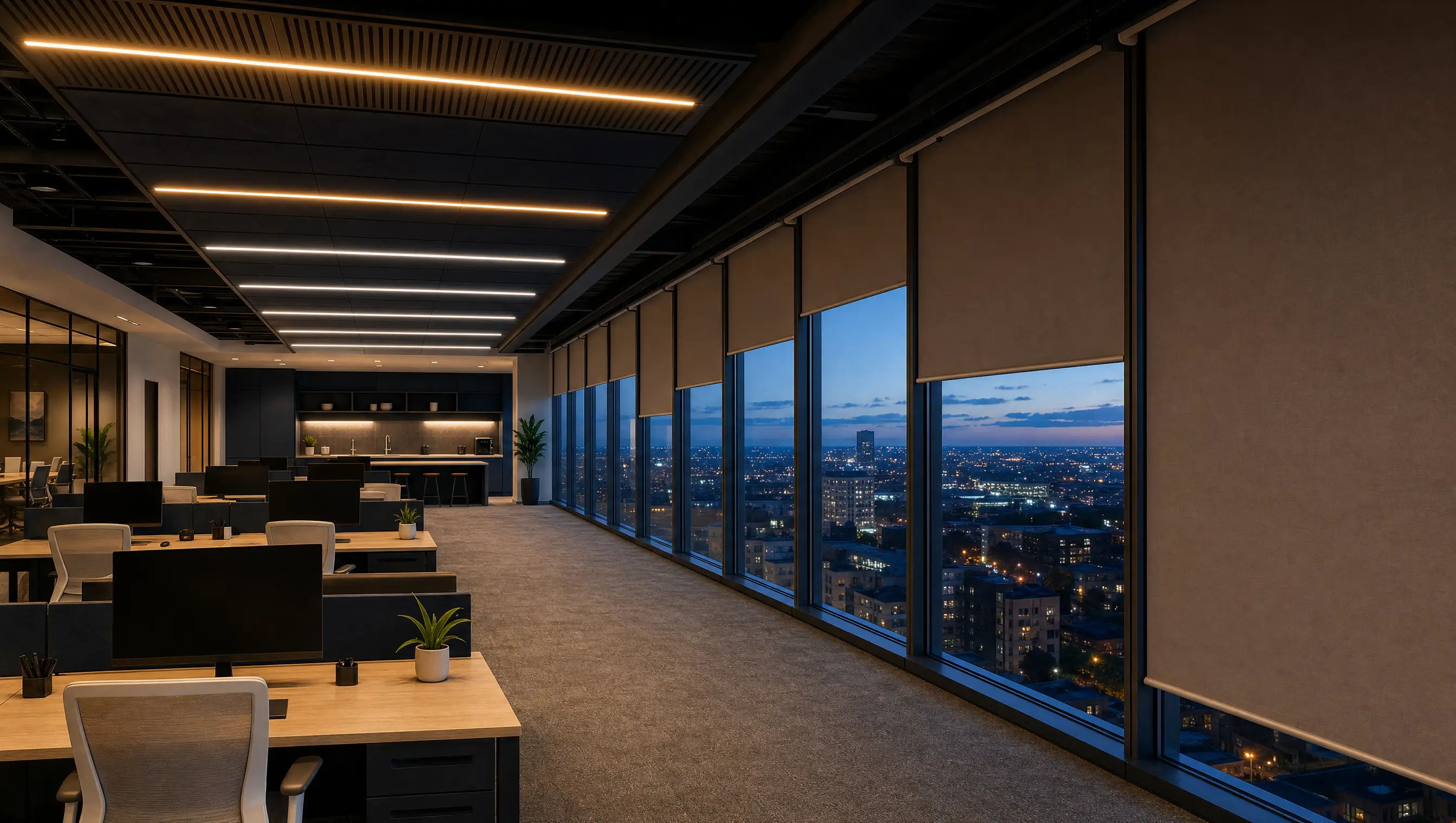 An open-plan office at dusk with motorised blinds descending in sequence and lighting zoned from warm to cool