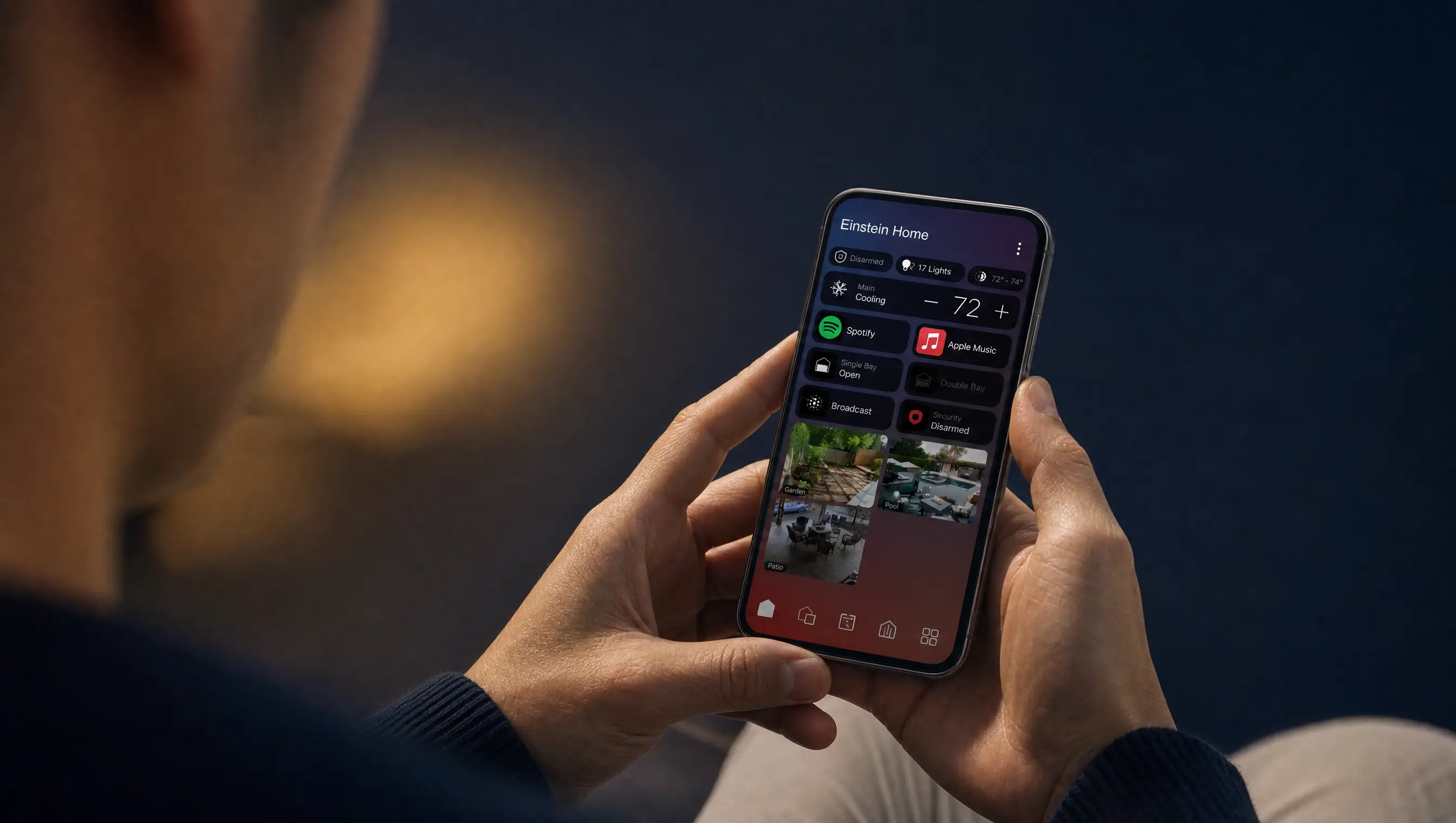 A person on a sofa in a navy living room at dusk, controlling the whole home from the Control4 app on their phone
